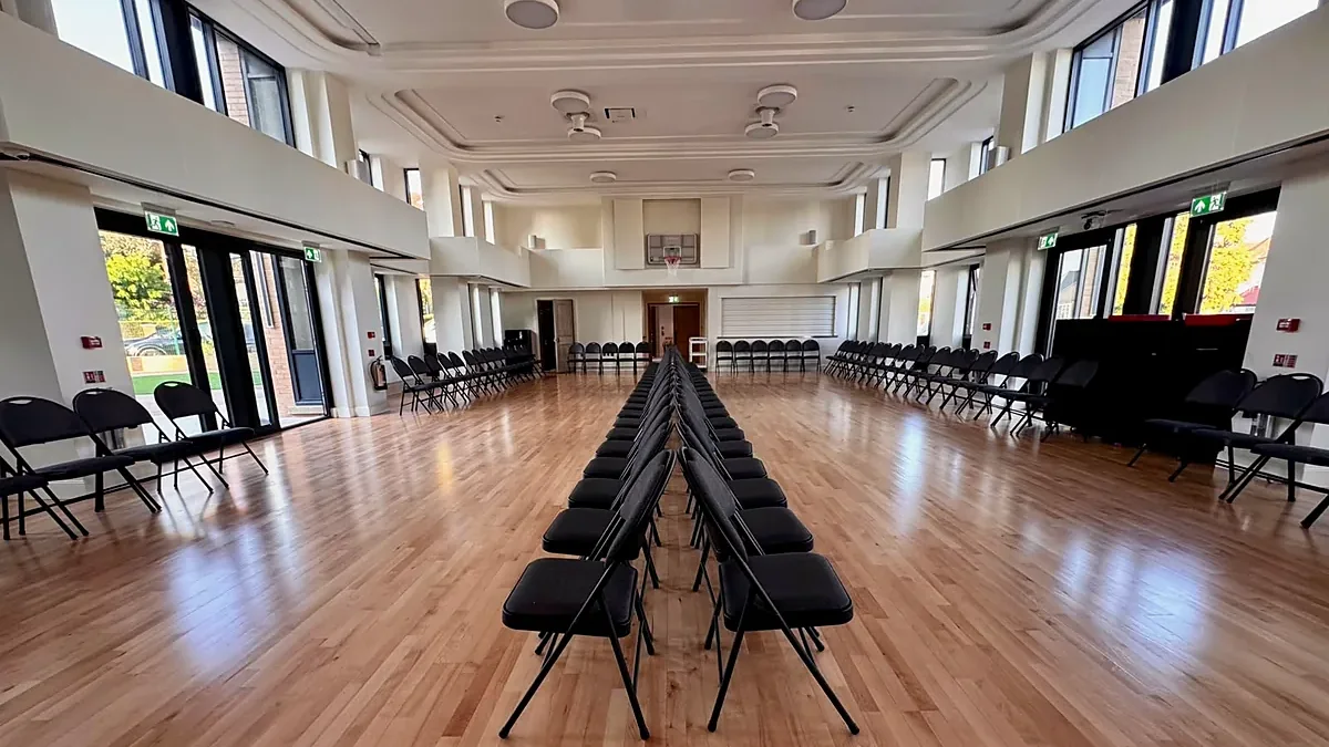 Father Michael Hall at The Ark in Golders Green, a double height hall with a coffered ceiling, galleries on both sides, full height windows and a polished timber floor set out with rows of chairs