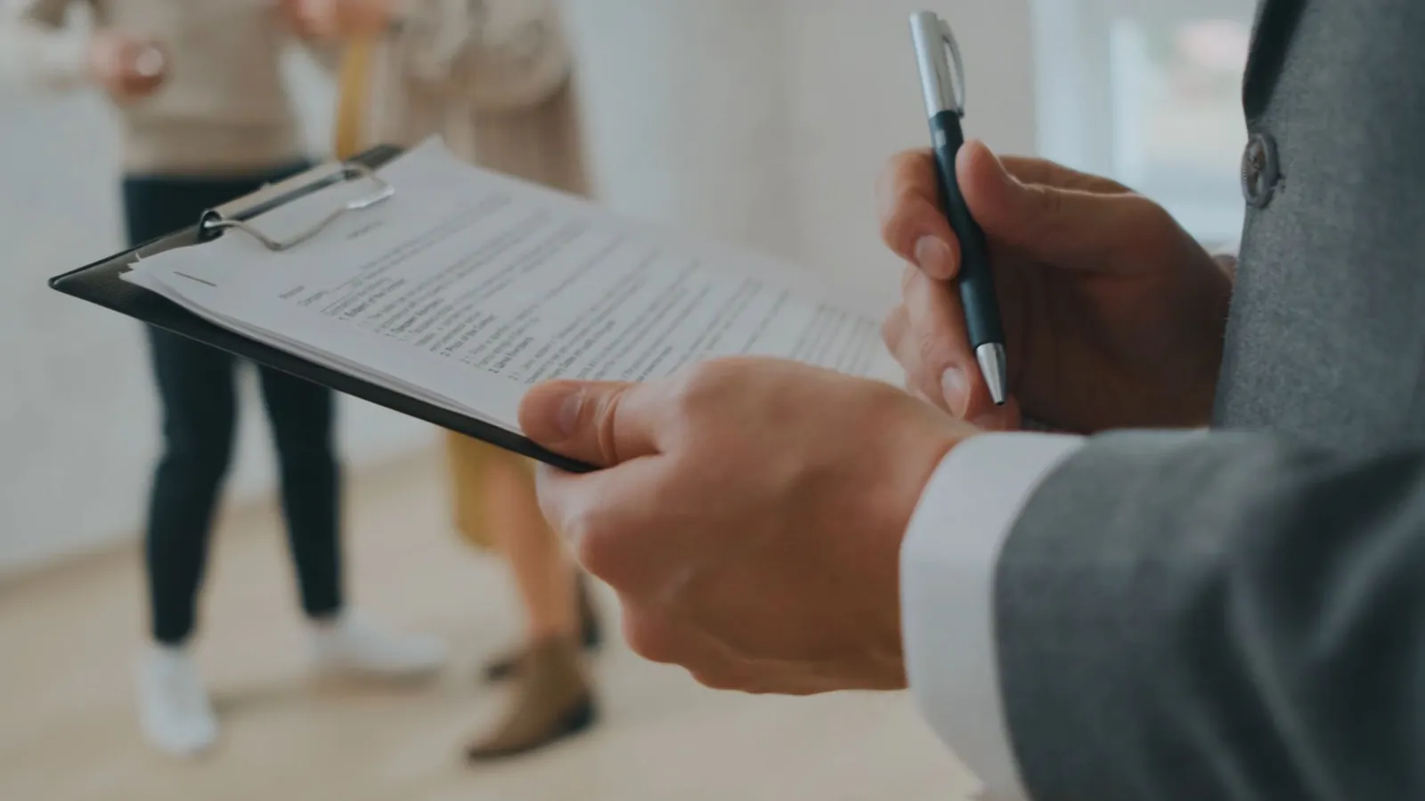 A letting agent holding a clipboard and pen during a property visit, recording the condition that decides fair wear and tear at the end of a tenancy
